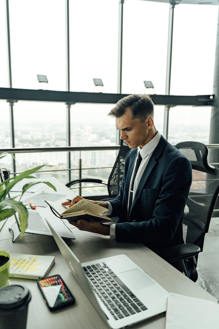 Businessman in black suit reading in a modern office with laptop.