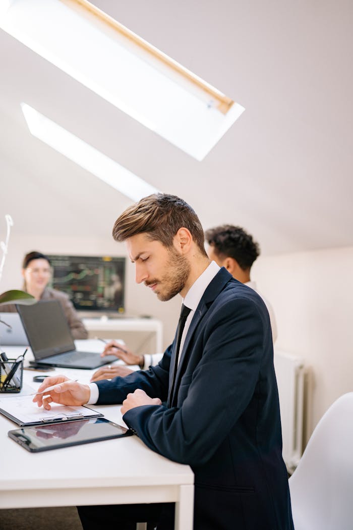 Business professionals in a modern office setting working on tablets and laptops, showcasing teamwork and productivity.